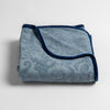 Adele Baby Blanket | Tahoe Blue | a folded blanket with the corner turned down to show the trim against a white background, shot from an overhead angle.