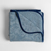 Adele Blanket | Tahoe Blue | folded organic cotton damask throw blanket shown with the corner folded down to show silk velvet trim detail — overhead against a plain white background.