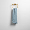 Austin Guest Towel | Tahoe Blue | midweight linen guest towel with raw edge band at both ends hanging from a towel ring mounted to a white wall.