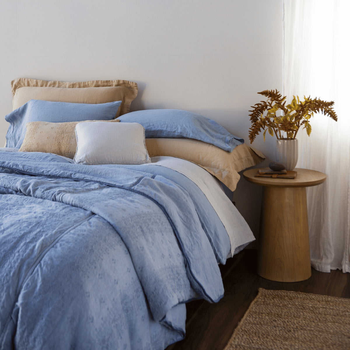 [allvariants]: Bedspread in tahoe blue with a variety of throw pillows and pillowcases in linen - close up angled view.