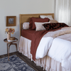 Lynette Luxe Duvet Cover | a pale pink duvet cover with dark terrcotta colored sheets and pillows against a rattan headboard with coordinating side table - shot from a 3/4 angle.