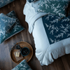 Lynette Luxe Duvet Cover | an overhead shot of a blue duvet cover with green and blue pillows scattered about the bed and dark wood floor.