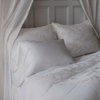 Lynette Luxe Duvet Cover | Winter White | duvet cover and matching shams shown with a silk and tencel™ pillowcase and white sheets — lighweight gauze curtain panels are draped around the head of the bed.