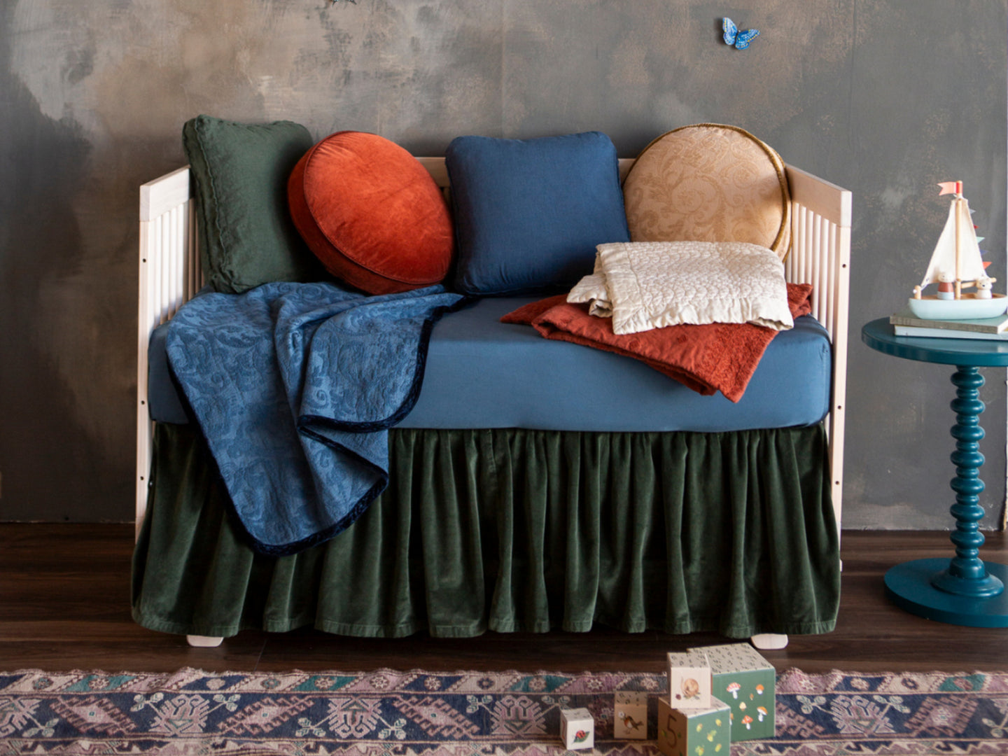 A colorful crib against a dark limewash wall with wooden childrens toys on the table and rug.