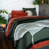 Cirillo Throw Pillow | Bold color combination shown on a bed in green and rust tones with plants around the head of the bed.