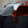 Loulah Throw Pillow | Autumn | a close up of a silk velvet bolster shown with grey and black bedding.