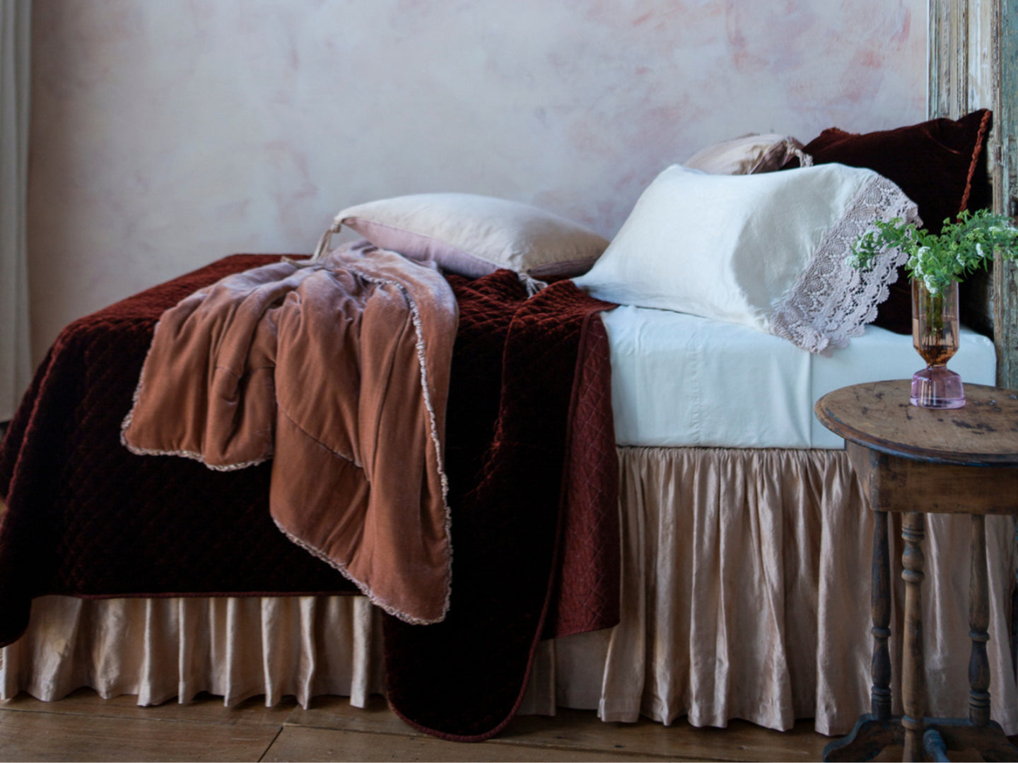 A bed shown from the side dressed in white, pinks and a rich terracotta tone in silk velvet. 