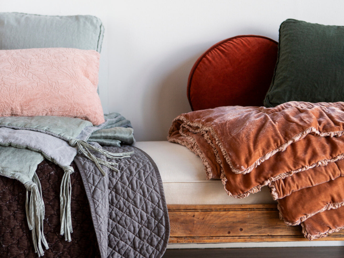 A bench with assorted throw pillows and blankets in lots of colors and textures. 