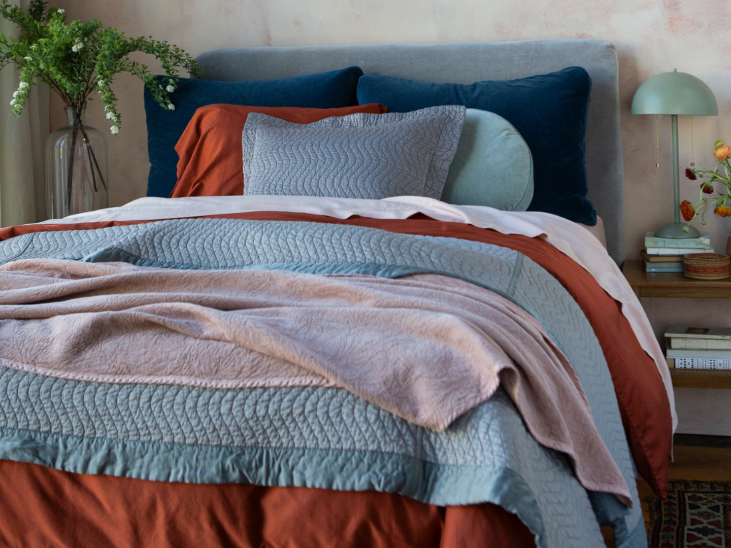 A colorful bed in pinks rust, dark blue and grey tones with lots of layers.