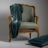 Carmen Blanket | Mineral | a matching throw blanket and throw pillow shown on an ornamental chair with moody lighting against a white background.