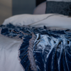 Loulah Blanket | Tahoe Blue | a close up of the blue silk velvet blanket rumpled at the foot of a bed also in blue tones and out of focus.