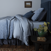 Madera Luxe Duvet Cover | a monochromatic bed in blue tones shown from the side with a side table holding a green vase and botanical.