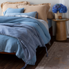 Taline Blanket | charmeuse blanket with tassesls on a plush linen bed in soothing blue and warm honey tones.