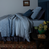 Vienna Sham | side view of a monochromatic bed in blue tones with a multi-colored rug and side table holding a bright green plant and books.