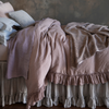 Linen Whisper Duvet Cover | side view of a bed dressed in mostly linen pieces in lavender and warm grey tones against a dark limewash wall with moody lighting.