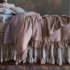Georgia Blanket | side view of a fully dressed bed in neutral toned linen bedding with ruffles on the pulled back duvet cover and bed skirt grazing the medium wood floor