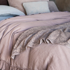 Georgia Blanket | the cotton jacquard side of the throw blanket is shown gently rumpled over a linen duvet cover with ruffle detailing. Throw pillows and shams are shown in the background of the shot at the head of the bed. 