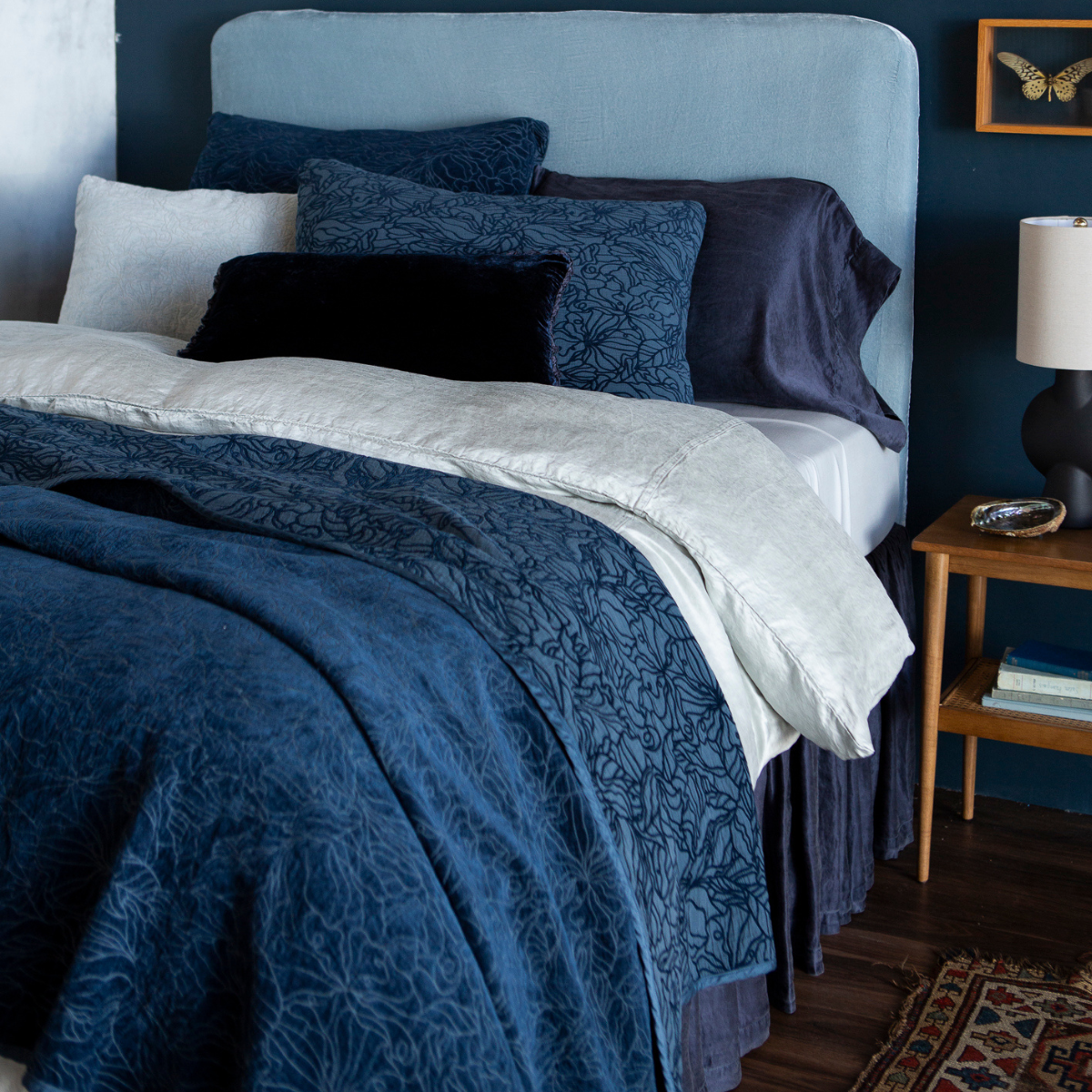 [allvariants]: shot at a three-quarter angle, the fully dressed bed is shown in blue tones in different fabrics showing the tonality and of the hues and pattern on the chenille and cotton jacquard bedspread and shams