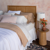 Georgia Twin Bedspread | a three-quarter view of a fully dressed bed in light tones with a rattan headboard against a pink-toned wall.