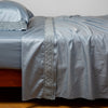 Bria Flat Sheet | Tahoe Blue | Cotton sateen sleeping pillow and flat sheet embellished with cotton lace trim on a bed - side view.