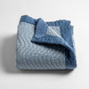 Cirillo Baby Blanket | Tahoe Blue | a folded quilted cotton sateen baby blanket with its corner folded down to show the trim contrast - shot against a white background.