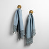 Two Frida guest towels, draped over decorative hooks against a white wall - tahoe blue.