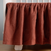 Autumn | A close-up side view of a crib with the Linen crib skirt in Autumn, a rich terracotta tone.