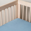 Madera Luxe Crib Sheet | Tahoe Blue | a blue tencel crib sheet shown into the corner of a natural wood crib.