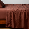 Madera Luxe Twin Flat Sheet | Autumn | A close-up side view of a bed with our Madera Luxe Flat Sheet and a matching pillowcase in Autumn, a rich terracotta tone.