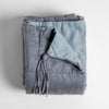 Taline Blanket | Tahoe Blue | a folded charmeuse blanket with its corner pulled back to reveal its midweight linen back and charmeuse tassel.